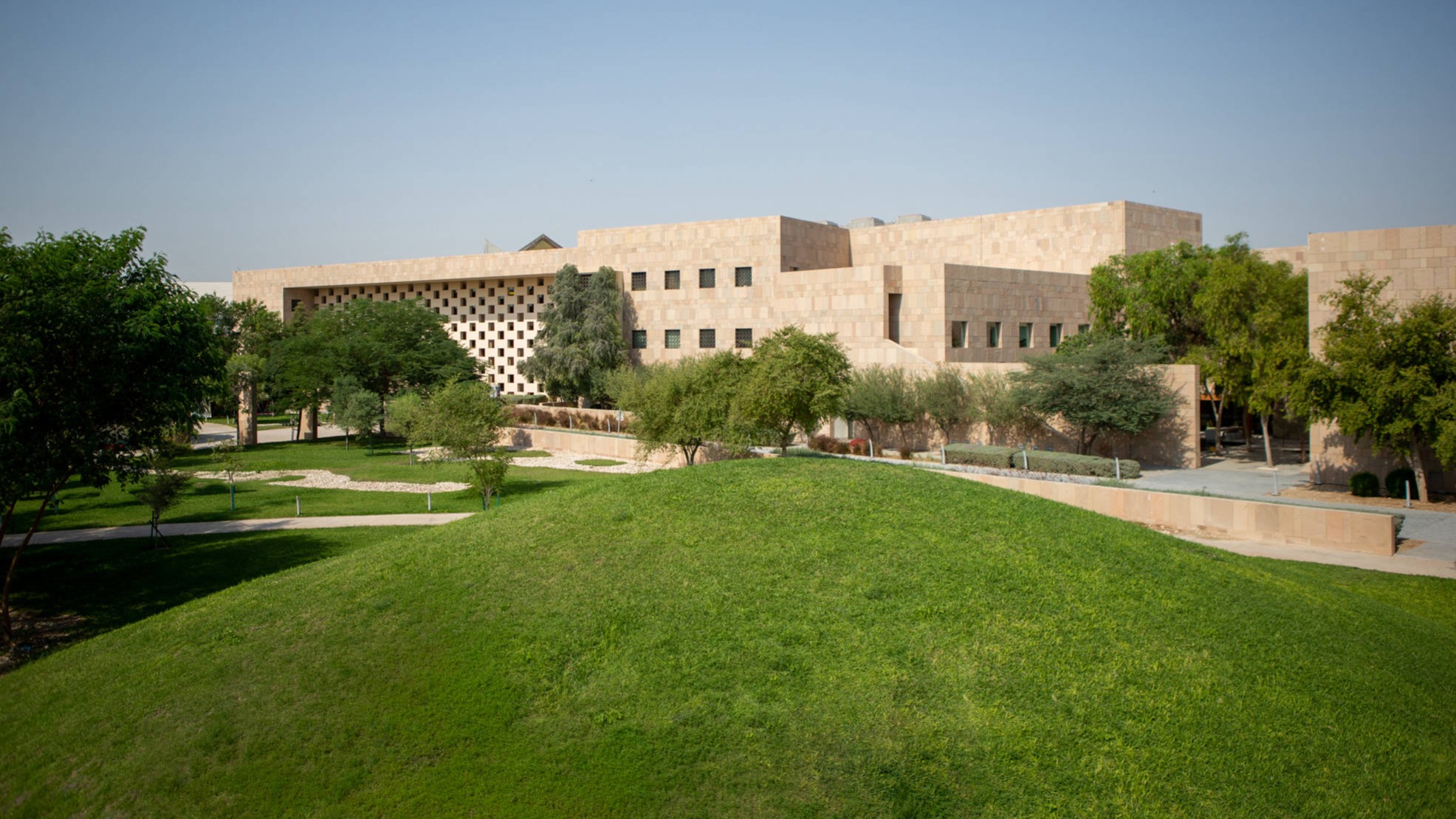 Exterior view of Georgetown University in Qatar showing green grassy hills and trees surrounding the building