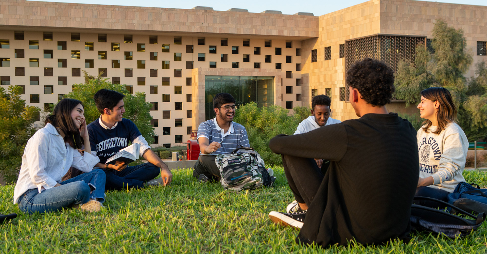 Students sitting in a circle on the grass outside the GU-Q building